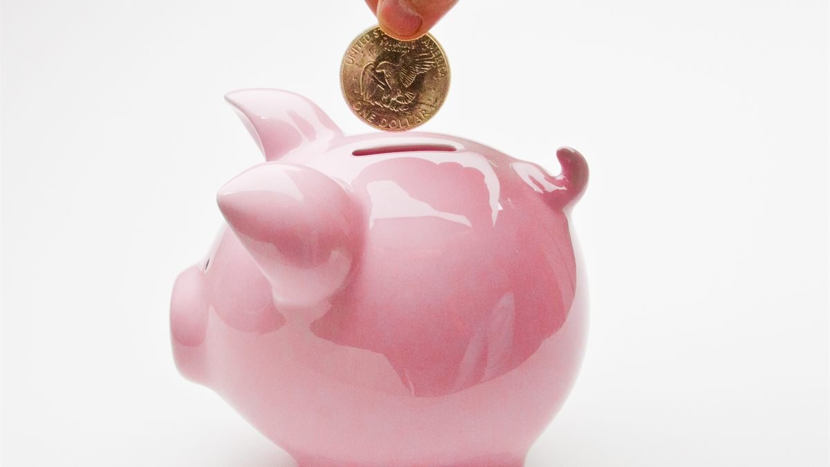A hand placing a coin into a piggy bank